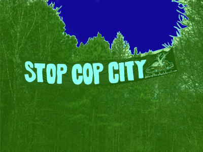 A 'Stop Cop City' banner over a forest background