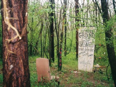 A chair in Weelaunee forest faces a sign which reads "On this ground GSP assassinated forest defender, comrade, friend, lover Tortuguita.